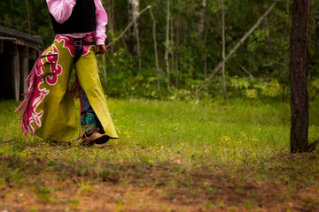 Fototapeta na wymiar The bottom torso of a young man in pink and green rodeo chaps and cowboy boots walking along a grass path