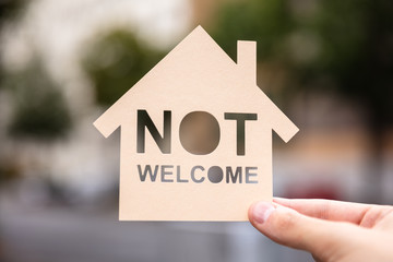 Hands Holding Paper With Cutout House And Non Welcome Words