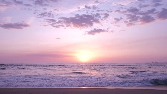 Wide shot over beach at sunset, parallel to shore. Slow zoom out. Beautiful pastel colors.
