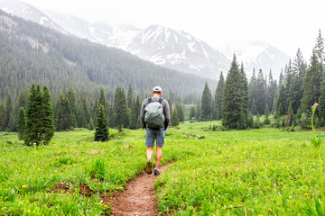 Open valley with man walking in rain on Conundrum Creek Trail in Aspen, Colorado in 2019 summer on cloudy day and dirt road