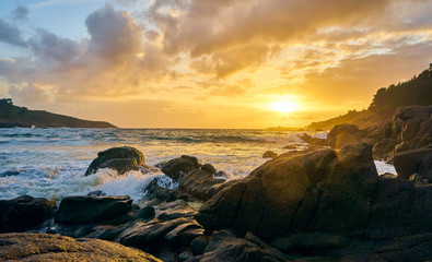 Sunset of the sea with rocks and mountain in the background. Beach and sea water with long exposure.