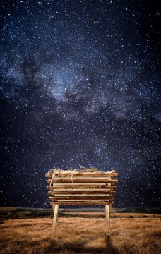 Old wooden cradle with hay in a field and under a starry sky