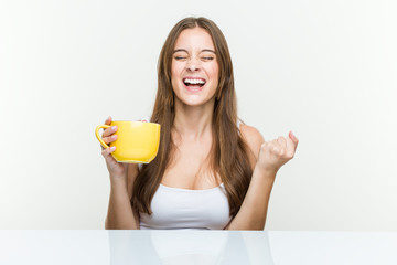 Young caucasian woman holding a cup cheering carefree and excited. Victory concept.