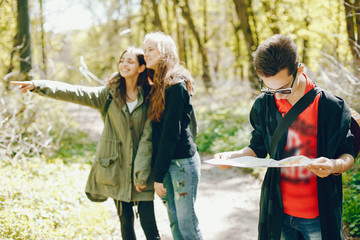 Three friends walking in a autumn forest. Tourists use the map. Boy and two girls have fun in a park