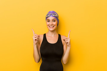Young swimmer caucasian woman indicates with both fore fingers up showing a blank space.