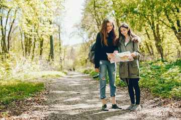 Obraz premium Two girls standing in a autumn forest. Friends have fun in a park. Tourists use the map.