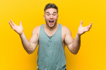 Young fitness man against a yellow background celebrating a victory or success, he is surprised and...