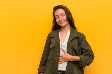 Young european woman isolated over yellow background touches tummy, smiles gently, eating and satisfaction concept.