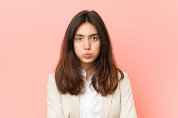 Fototapeta premium Young brunette business woman against a pink background blows cheeks, has tired expression. Facial expression concept.