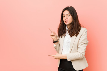 Young brunette business woman against a pink background shocked pointing with index fingers to a copy space.