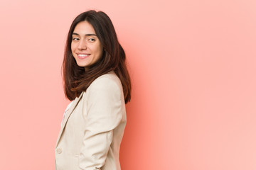 Fototapeta premium Young brunette business woman against a pink background looks aside smiling, cheerful and pleasant.