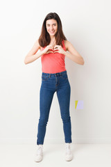 Full body young woman on white background smiling and showing a heart shape with hands.