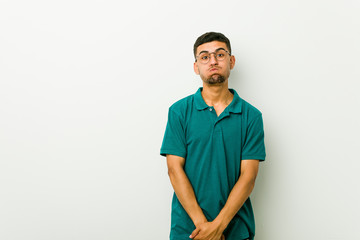 Fototapeta premium Young hispanic man blows cheeks, has tired expression. Facial expression concept.