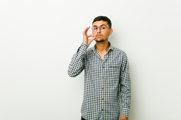 Young hispanic man with fingers on lips keeping a secret.