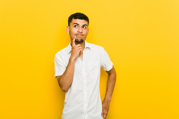 Young hispanic man looking sideways with doubtful and skeptical expression.