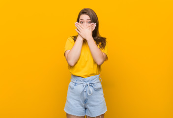 Young woman teenager wearing a yellow shirt shocked covering mouth with hands.