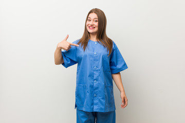 Young nurse woman against a white wall person pointing by hand to a shirt copy space, proud and confident