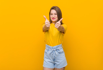 Young woman teenager wearing a yellow shirt with thumbs ups, cheers about something, support and respect concept.