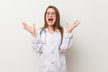 Young doctor woman against a white wall celebrating a victory or success, he is surprised and shocked.