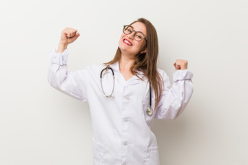 Young doctor woman against a white wall raising fist after a victory, winner concept.