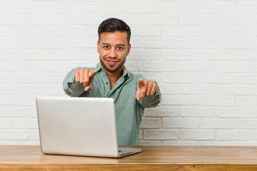 Young filipino man sitting working with his laptop cheerful smiles pointing to front.