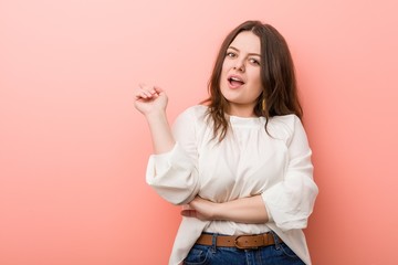 Young caucasian curvy woman standing against pink background