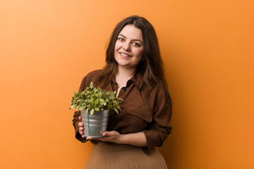 Young curvy plus size woman holding a plant happy, smiling and cheerful.