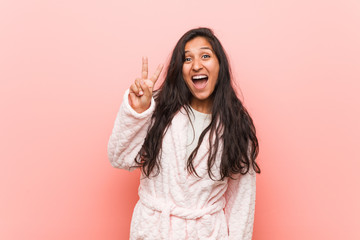 Young indian woman wearing pajama showing victory sign and smiling broadly.