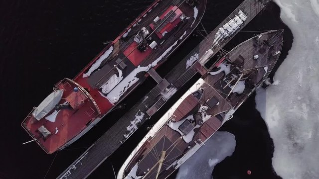 Old wooden museum boats at dock in winter. Vertical aerial rising shot.