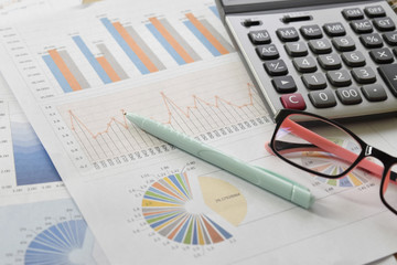 Obraz premium Financial graphs and charts with glasses, calculator on desk.