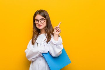 Little caucasian girl wearing a doctor costume smiling cheerfully pointing with forefinger away.