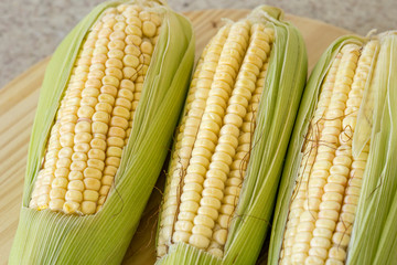 Closeup of raw corn cobs with straw over wood