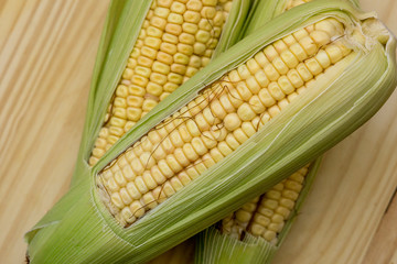 Closeup of raw corn cobs with straw over wood