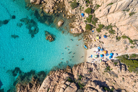 View from above, stunning aerial view of a small beach with beach umbrellas and people swimming in a turquoise clear water, Cala Coticcio, (Tahiti), La Maddalena Archipelago, Sardinia, Italy.