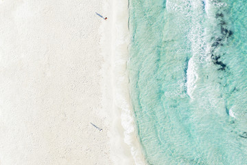 View from above, stunning aerial view of two people walking a white beach bathed by a beautiful turquoise clear water. Emerald Coast Sardinia, Italy.