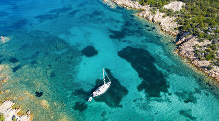 View from above, stunning aerial view of a sailboat floating on a beautiful turquoise sea that bathes the green and rocky coasts of Sardinia. Emerald Coast Italy