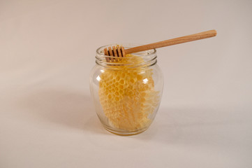 Frame with sealed honey, a glass jar with golden honey and a wooden spoon for mixing and tasting natural honey