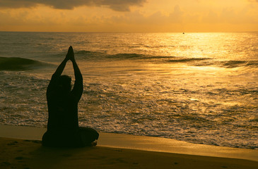  Indian woman meditating on morning sunrise beach
