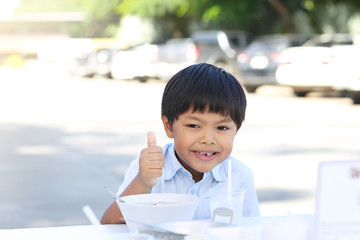An Asian boy eating rice congee with minced pork, boiled egg and vegetable in white ceramic bowl.