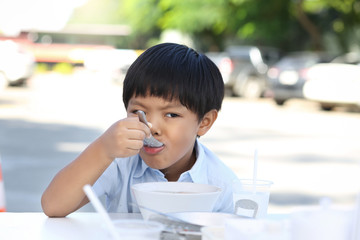 An Asian boy eating rice congee with minced pork, boiled egg and vegetable in white ceramic bowl.