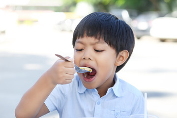 An Asian boy eating rice congee with minced pork, boiled egg and vegetable in white ceramic bowl.