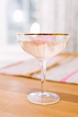 Romantic pink bubbly sparkling cocktail made with champagne, vodka, and rose water, shaken with ice, served in gold rimmed coupe glass, garnished with rose petal.
