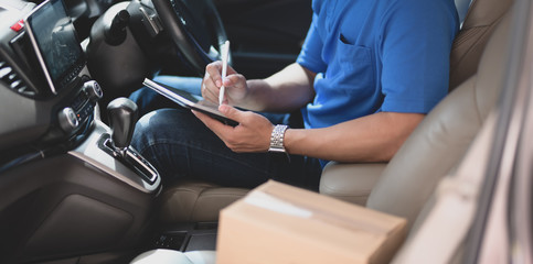 Young delivery man checking the products to customer with tablet while sitting on the car