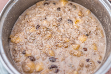 Closeup of oatmeal oat grain pudding porridge in cooking pot with chopped banana slices and raisins