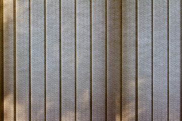 Beige color vertical blinds abstract texture background with light filtering outdoor tree shadows and silhouettes and bokeh