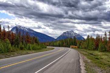 yellow bus on the road among the Rocky mountains.  picturesque cloudy sky. Beautiful views of Icefields Parkway in Jasper National Park, Alberta, Canada