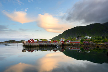 Fototapeta premium Fishing boat and red village Reflecting the water in the evening at Ballstad, Northern Norway, Rorbu is the traditional home of Norwegian fishermen.
