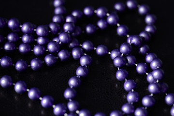 Long beaded necklace purple color on a dark background close up