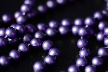 Long beaded necklace purple color on a dark background close up