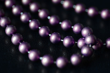 Long beaded necklace purple color on a dark background close up